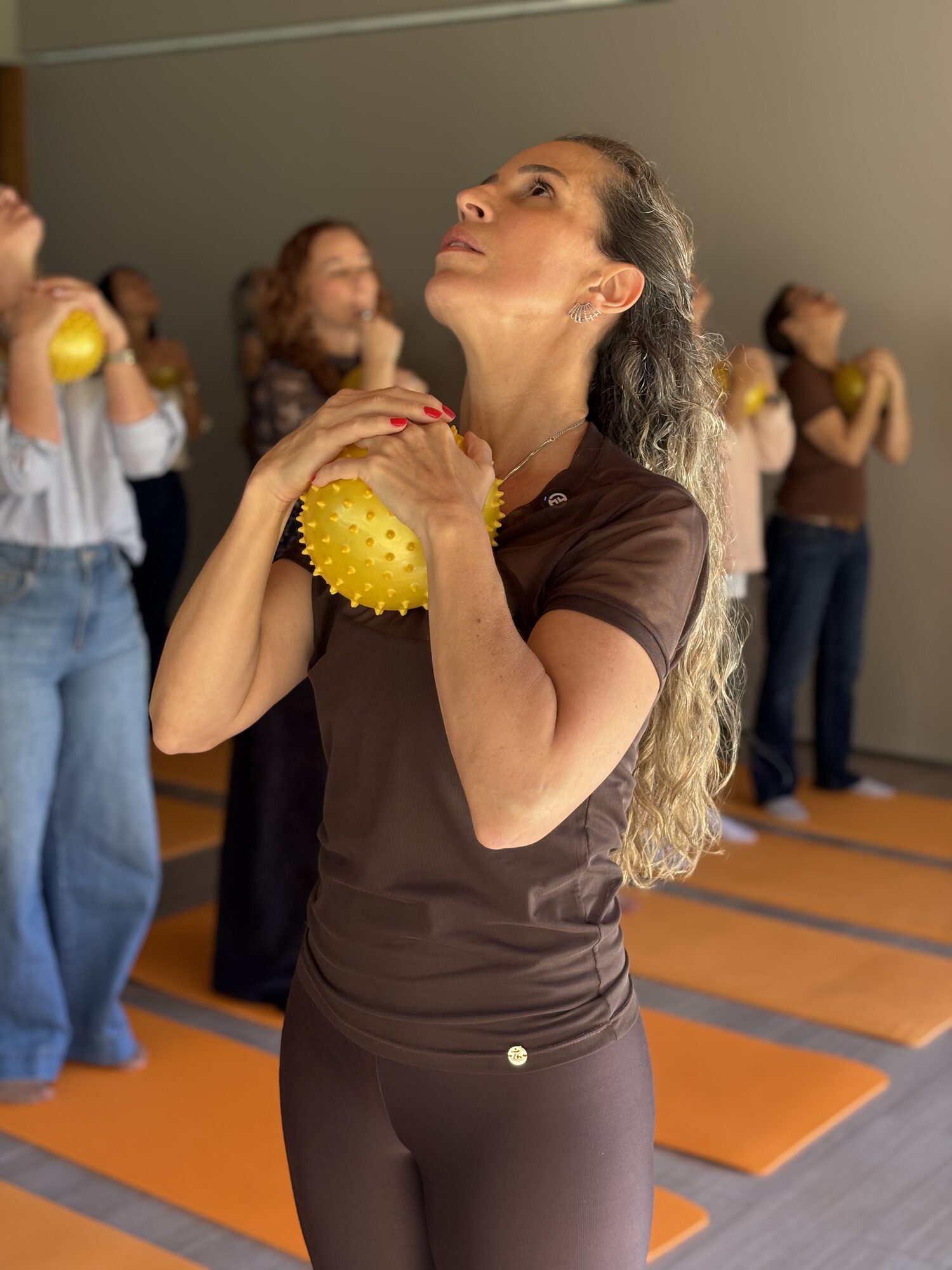 Mulher em pé segurando bolinha laranja próximo ao rosto em gesto de meditação