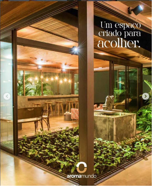 Interior aberto da Casa Aromamundo, com vidro, madeira e vegetação
